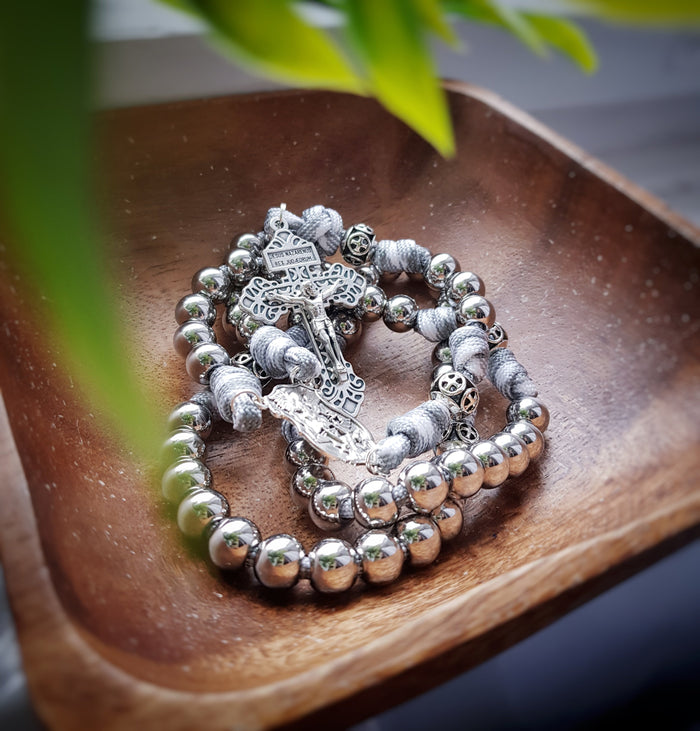 Erzengel-Michael-Rosenkranz aus grau-weißem Paracord mit Edelstahlperlen und Pardon-Kruzifix in einer Holzschale